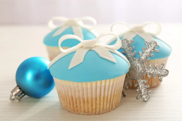 Cupcakes saborosos com arco e brinquedos de Natal na cor de fundo de madeira — Fotografia de Stock