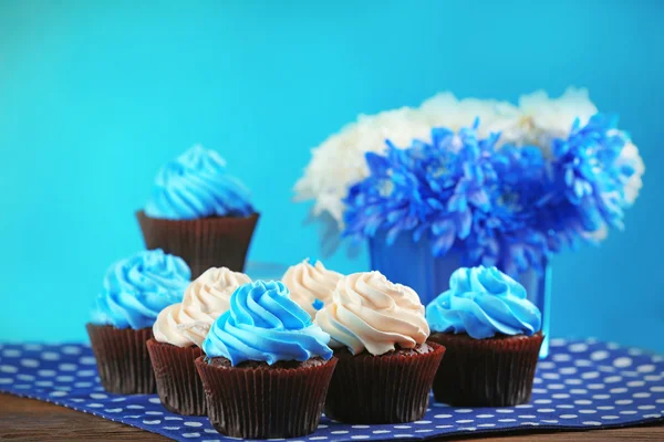 チョコレートのカップケーキと青い背景の前で木製のテーブルの上に花 — ストック写真