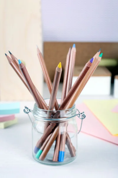 Set med färgade pennor i glas kruka på en tabell — Stockfoto