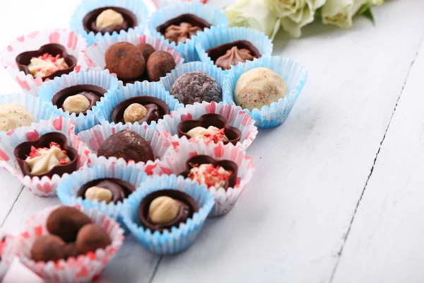 Ensemble de bonbons au chocolat avec des fleurs sur un fond en bois clair, gros plan — Photo