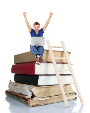 Adam kitap yığını üzerinde oturan dizüstü bilgisayar ile