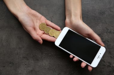 Madeni para ile akıllı telefon gri arka plan üzerinde holding eller. Telefon masrafları