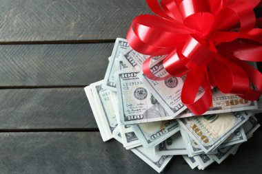 Ahşap arka plan üzerinde hediye olarak yay ile dolar yığını