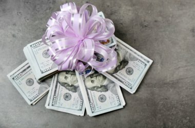 Gri dokulu arka plan üzerinde hediye olarak yay ile dolar yığını