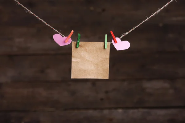 Paper hearts and empty sheet hanging on cord against wooden background — Stock Photo, Image