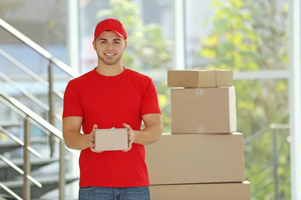 Postbote in roter Uniform hält Paket — Stockfoto