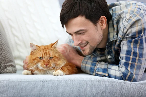 Jovem com gato fofo deitado em um sofá — Fotografia de Stock