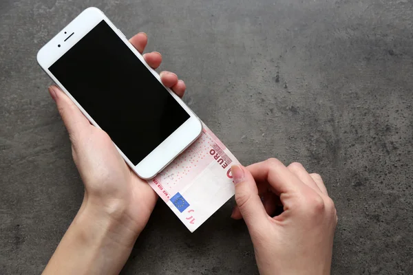 Handen met slimme telefoon met euro biljet op grijze achtergrond. Maken van geld online — Stockfoto