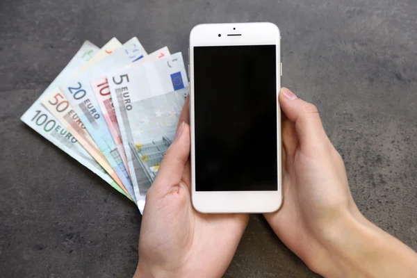 Manos con teléfono inteligente y billetes en euros sobre fondo gris. Ganar dinero en línea —  Fotos de Stock