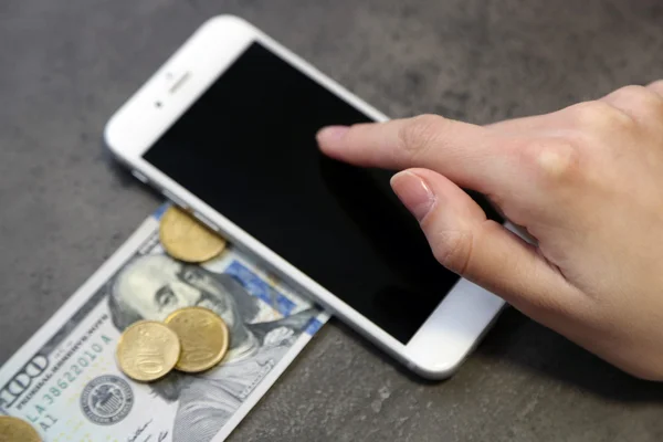 Mano con smart phone, banconote in dollari e monete su sfondo grigio. Spese telefoniche — Foto Stock