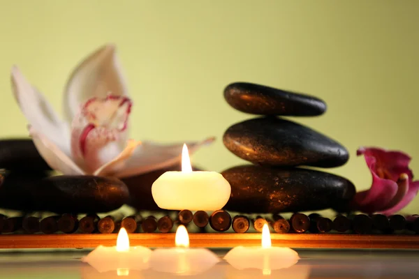 Спа натюрморт с камнями, свечами и цветами в воде на зеленом размытом фоне — стоковое фото