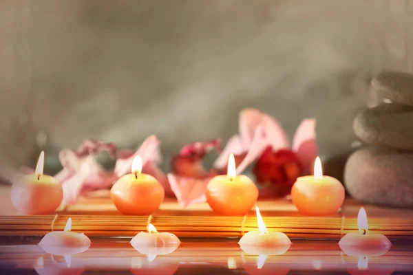 Bodegón Spa con piedras, velas y flores en agua sobre fondo gris — Foto de Stock