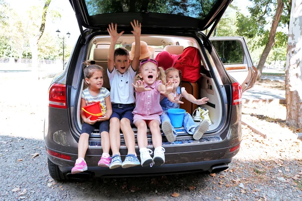 Šťastné děti sedí na kufru auta — Stock fotografie