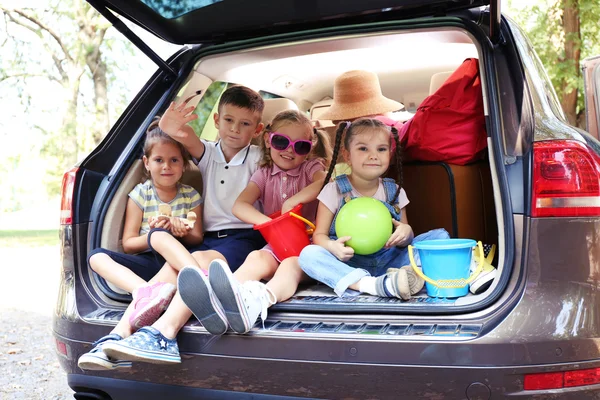 Three beautiful girls and boy sit on a car trunk and laughing — Stock Photo, Image