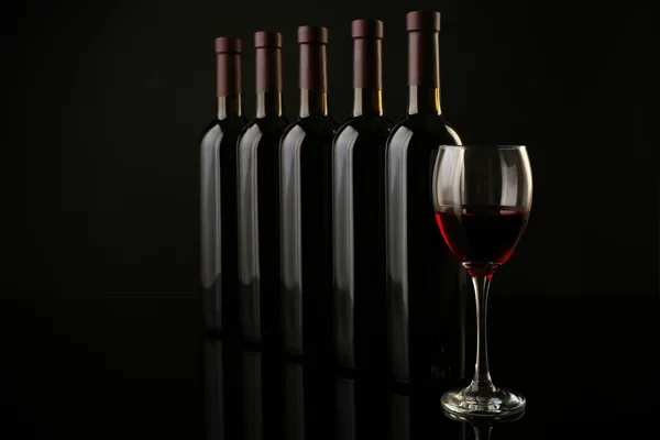 Copo de vinho tinto contra garrafas — Fotografia de Stock