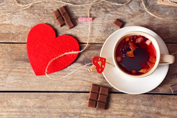 Taza de té con corazón rojo y trozo de chocolate sobre fondo de madera —  Fotos de Stock