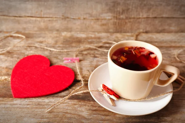 Cup of tea with red heart and rope with clothespins on wooden background closeup — Stock Photo, Image