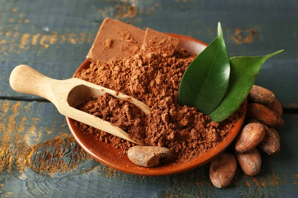 Schüssel mit aromatischem Kakaopulver und grünem Blatt auf zerkratztem Holzgrund, Nahaufnahme — Stockfoto