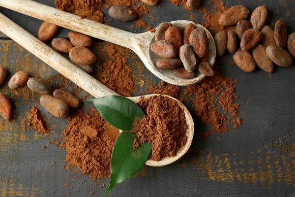 Lingură cu pudră de cacao aromatică și frunze verzi pe fundal din lemn zgâriat, închide — Fotografie, imagine de stoc