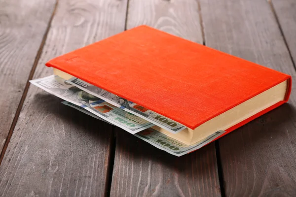 Red book with nested dollar banknotes on wooden table. Stash of money — Stock Photo, Image