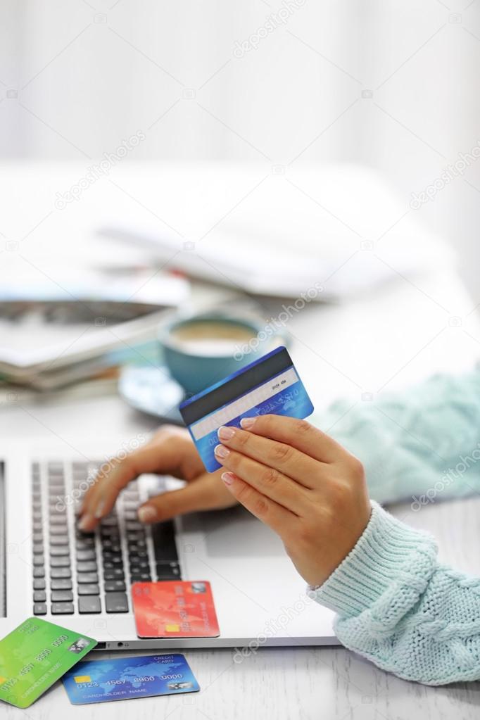 E-commerce concept. Woman with credit card, laptop and cup of coffee, close up