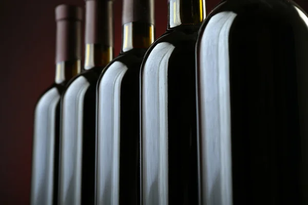 Κρασιού μπουκάλια σε μια γραμμή σε σκούρο κόκκινο φόντο, κοντινό πλάνο — Φωτογραφία Αρχείου