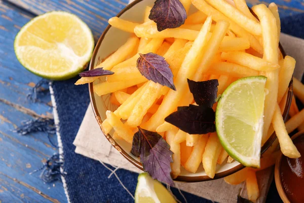 Batatas fritas francesas em tigela com manjericão e molho no fundo de madeira velho — Fotografia de Stock