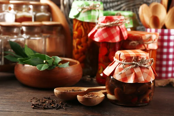 Jars with pickled vegetables, beans, spices and kitchenware on wooden background — Stock Photo, Image