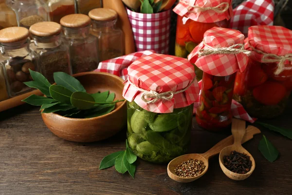 Frascos con verduras y frijoles en escabeche, especias, libro de recetas y utensilios de cocina sobre fondo de madera — Foto de Stock