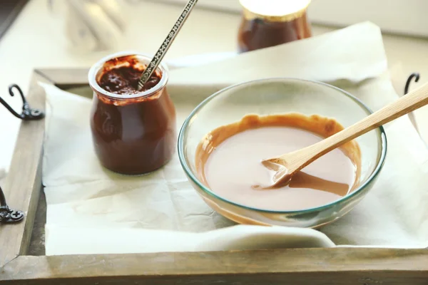 Chocolate derretido en cuenco de vidrio en bandeja, sobre fondo de madera — Foto de Stock