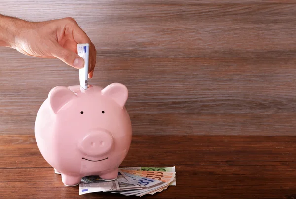 Man putting banknote in pig moneybox — Stock Photo, Image