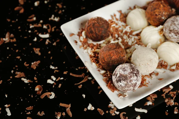 Siyah arka plan üzerinde pul ile beyaz plaka üzerinde çeşitli çikolata şekerleme — Stok fotoğraf