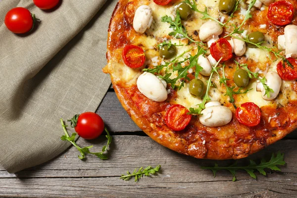 Deliciosa pizza, verduras frescas y servilleta de algodón sobre fondo de madera, de cerca —  Fotos de Stock
