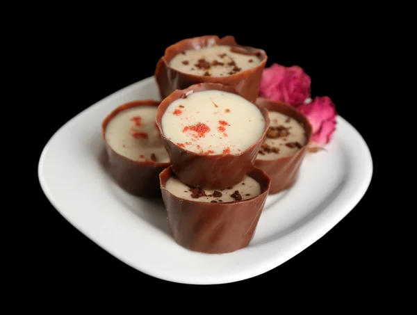 Verschiedene Schokoladenbonbons auf weißem Teller über schwarzem Hintergrund — Stockfoto