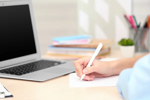 Frau macht sich mit Laptop Notizen auf einem Blatt Papier — Stockfoto