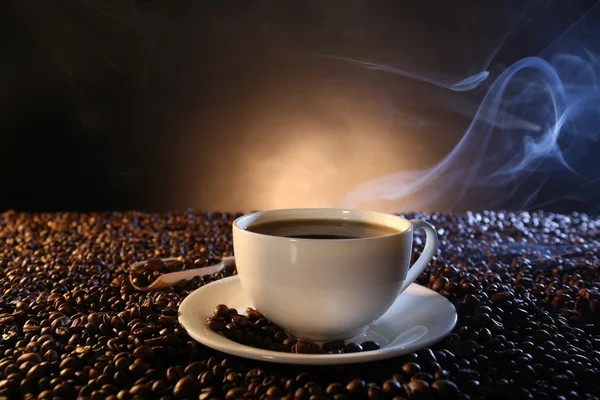 Cup of hot coffee among coffee beans on dark background Stock Photo