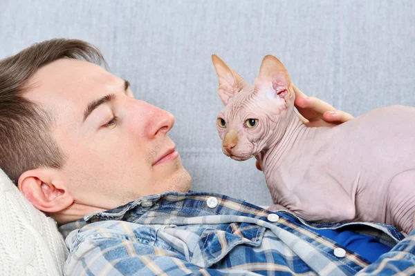 Pohledný muž leží s kočkou na gauči — Stock fotografie