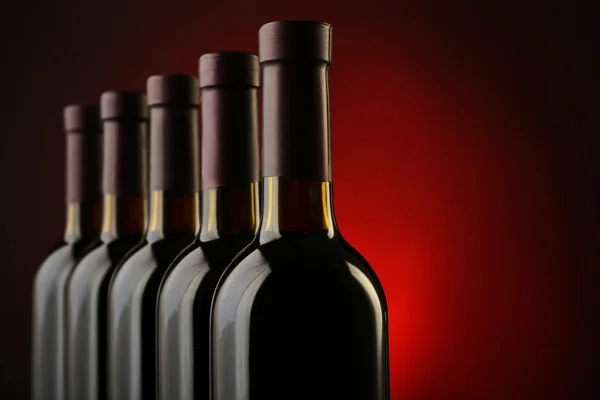 Bottiglie di vino in fila su sfondo rosso scuro, da vicino — Foto Stock