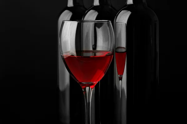 Red wine glass against bottles in a row on black background, close up — Stock Photo, Image