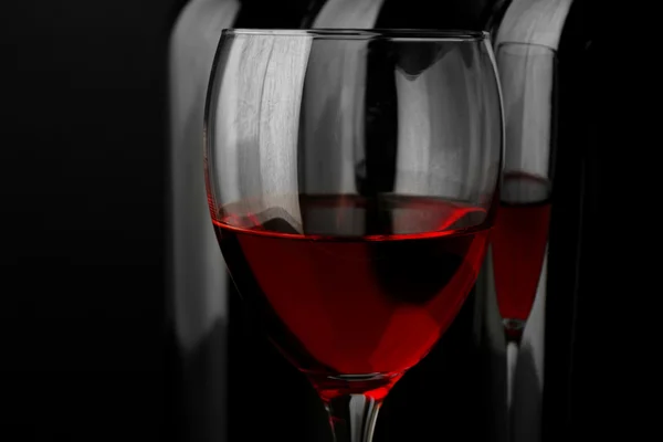 Kieliszek do wina czerwonego przeciwko butelek z rzędu na czarnym tle, z bliska — Zdjęcie stockowe