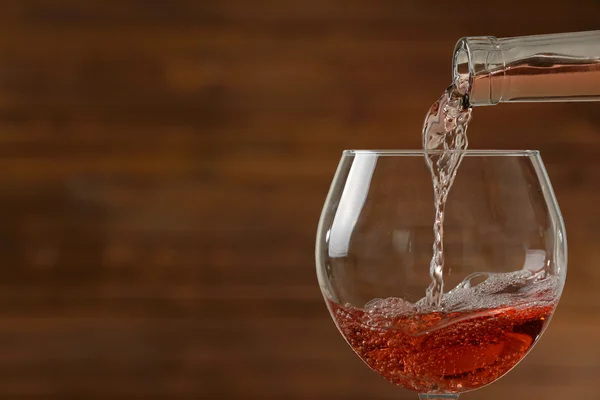 Vino rosato versato in vetro su fondo di legno — Foto Stock