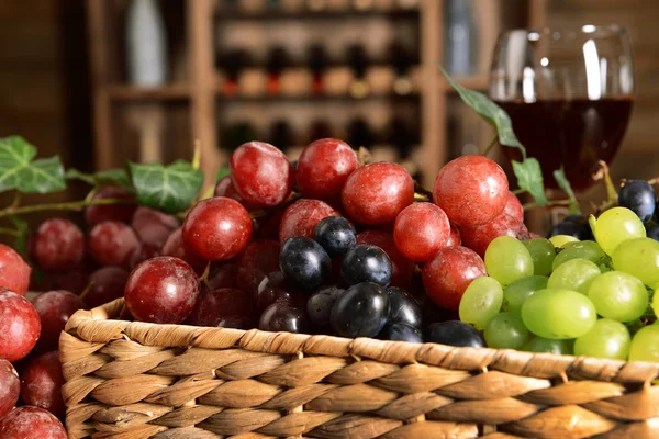 枝編み細工品ボックス ワインのボトルの背景にテーブルの上のブドウ — ストック写真