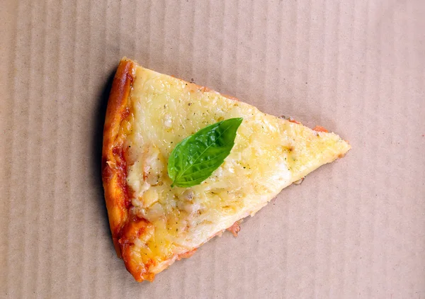 Smakelijke segmenten van pizza met basilicum op karton, close-up — Stockfoto