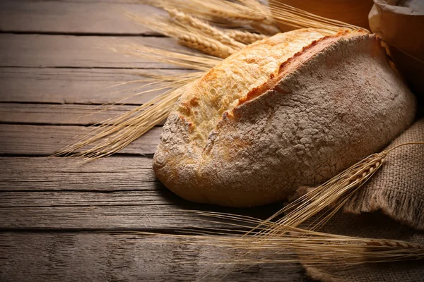 Pão fresco assado e trigo no fundo de madeira — Fotografia de Stock