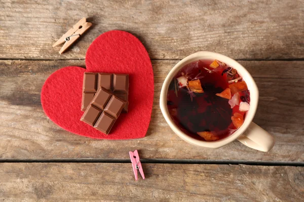 Чашка чая с кусочком шоколада на красном сердце и прищепки на деревянном фоне крупным планом — стоковое фото