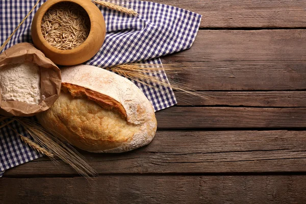 Pane appena sfornato, farina, grano e tovagliolo sullo sfondo di legno — Foto Stock