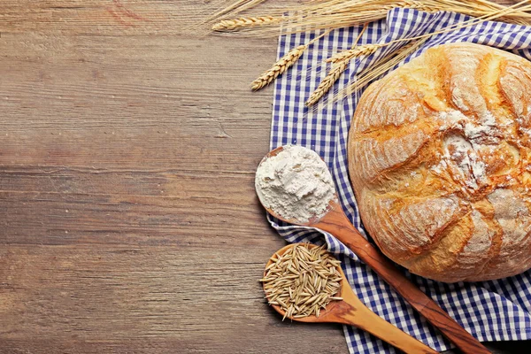 Čerstvě upečený chléb, mouka, pšeničný lžíce a ubrousek na dřevěné pozadí — Stock fotografie