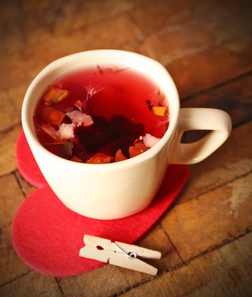 Чашка фруктового чая на красном сердце с прищепкой на деревянном фоне крупным планом — стоковое фото