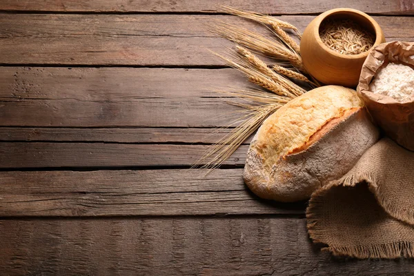 Pan recién horneado, harina y trigo en el fondo de madera — Foto de Stock