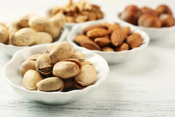 Pistacchi, mandorle, arachidi, gherigli di noci e nocciole nelle ciotole sul tavolo di legno bianco, primo piano — Foto Stock